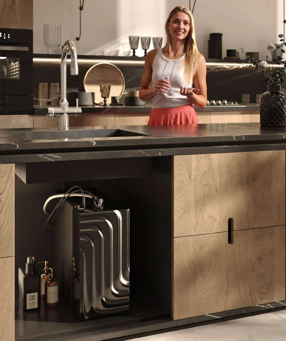 A view into a kitchen: the slim WaveHome box stands in the base cabinet next to the sink, a woman with a glass of water in the background.